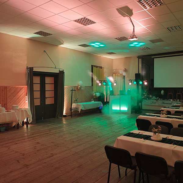 DJ-Pult mit blauer LED-Beleuchtung, zwei Lichtstativen und Lautsprechern in rustikaler Scheune mit Holzbalken, Backsteinwand und Ballondekoration 