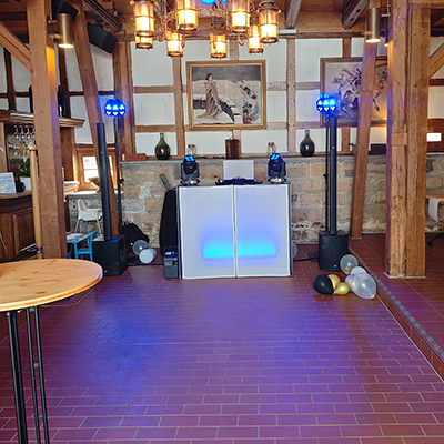 Aufgebautes DJ-Pult mit blauer LED-Beleuchtung in einer rustikal renovierten Scheune mit Holzbalken, Backsteinwand und Partyballons – Hochzeitsfeier mit DJ Oberhof