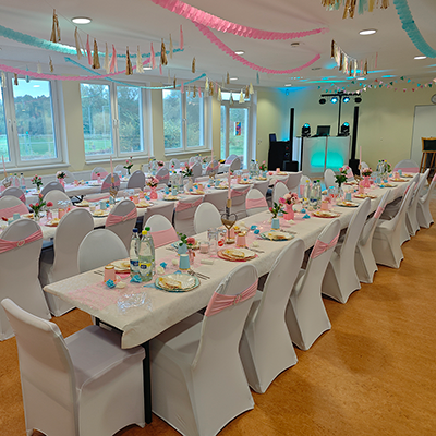 festlich dekorierte Tische mit weißen Hussen und rosa-blauer Dekoration, DJ-Pult mit Lichttechnik im Hintergrund