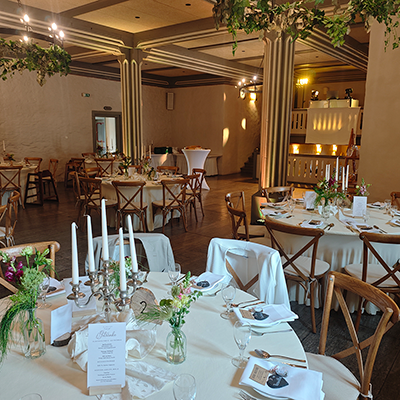Festsaal eines Ritterguts bei Mühlhausen mit markanter Holzbalkendecke während einer Hochzeit. Im Vordergrund stehen weiß gedeckte Tische; im Hintergrund befindet sich das weiße, beleuchtete DJ-Pult von DJ Andreas mit Säulenlautsprechern und Moving-Heads.