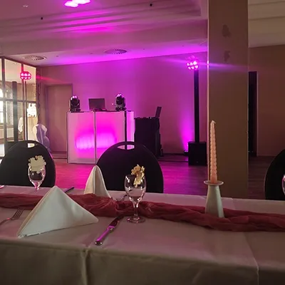 Gedeckter Hochzeitstisch im Vordergrund und pink beleuchtetes Technikpult für eine Hochzeit mit DJ Gerstungen in einem Schlosssaal